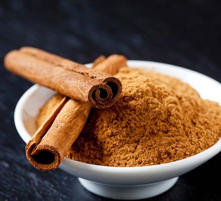 Bowl of cinnamon powder and two cinnamon sticks